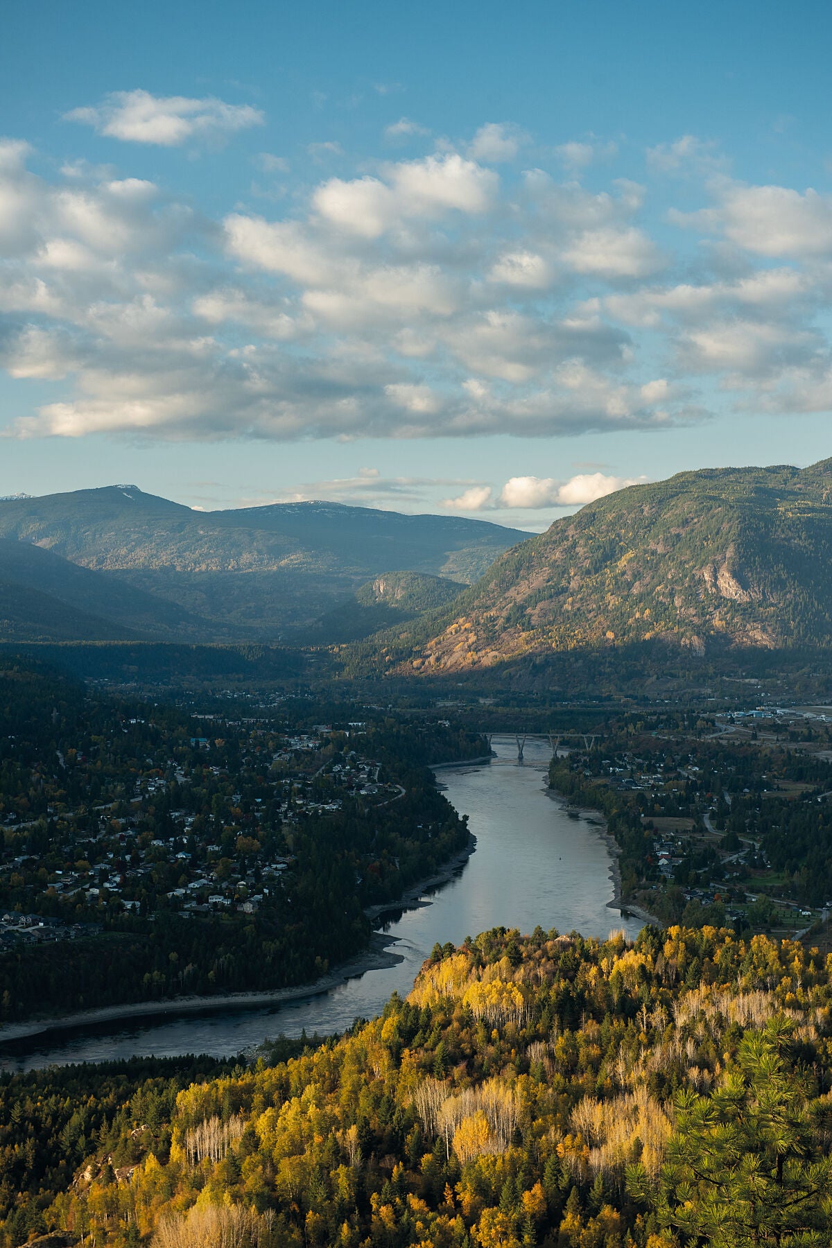 A scenic view of Castlegar, British Columbia, with the Columbia River winding through the town and mountains in the background, captured during autumn. Landscape photography by Ashley Voykin.