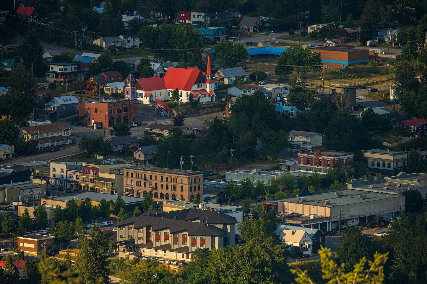 A telephoto view of Rossland, British Columbia, showing the town's downtown area with buildings, trees, and historic church, West Kootenay landscape photography by Ashley Voykin.