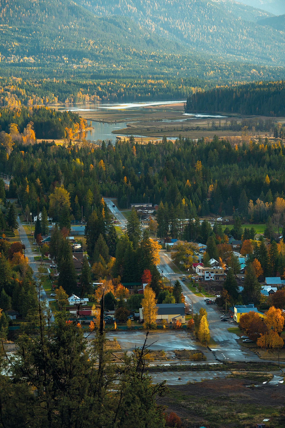 A scenic view of Slocan City with fall colours, including red and yellow leaves on the trees, and the Slocan River in the Distance. West Kootenay fine art photography by Ashley Voykin.