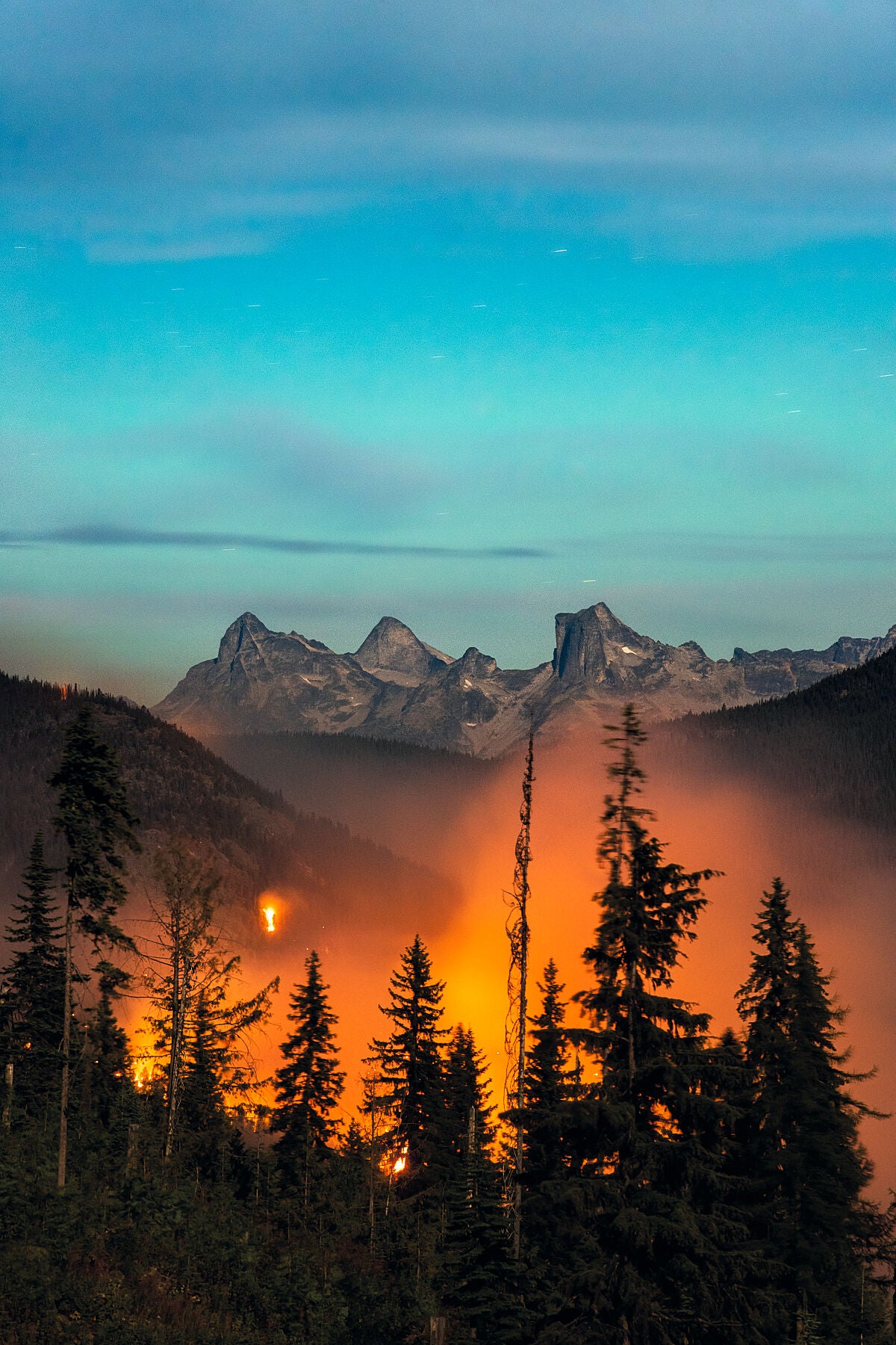 The Talbot Creek Wildfire burning at night, with the Valhalla Mountain Range visible behind. Environmental photography by Ashley Voykin.