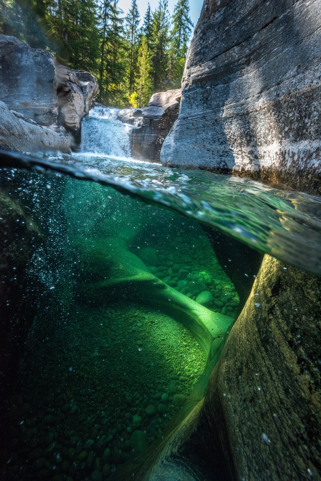 Underwater through a rocky pool, a waterfall in the background and bubbles in the foreground. A flowing creek near Castlegar, British Columbia.