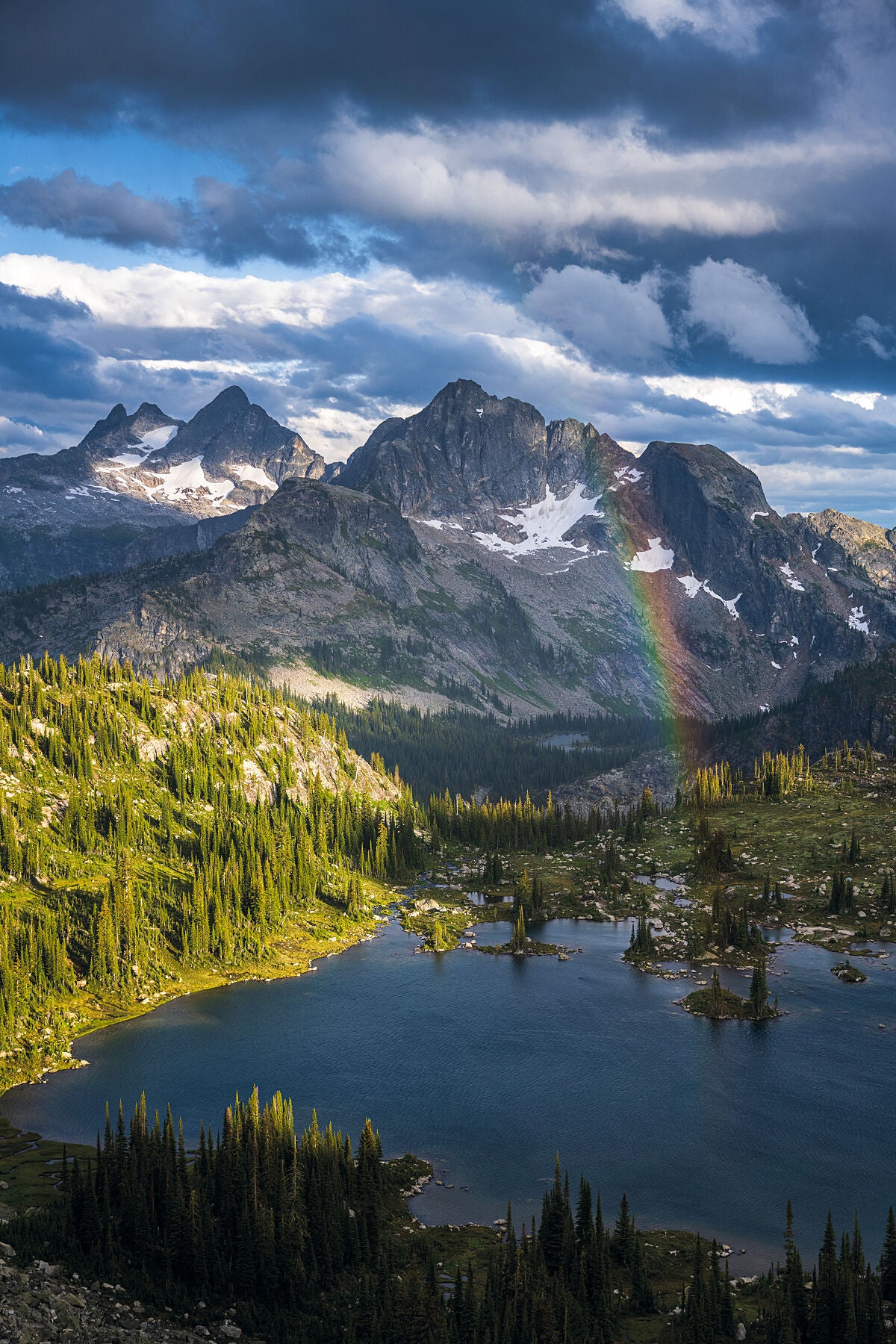 Storm clouds and a rainbow over Gwillim Lakes in Valhalla Provincial Park, during the Summer hiking season. Backcountry fine art landscape print by Ashley Voykin.