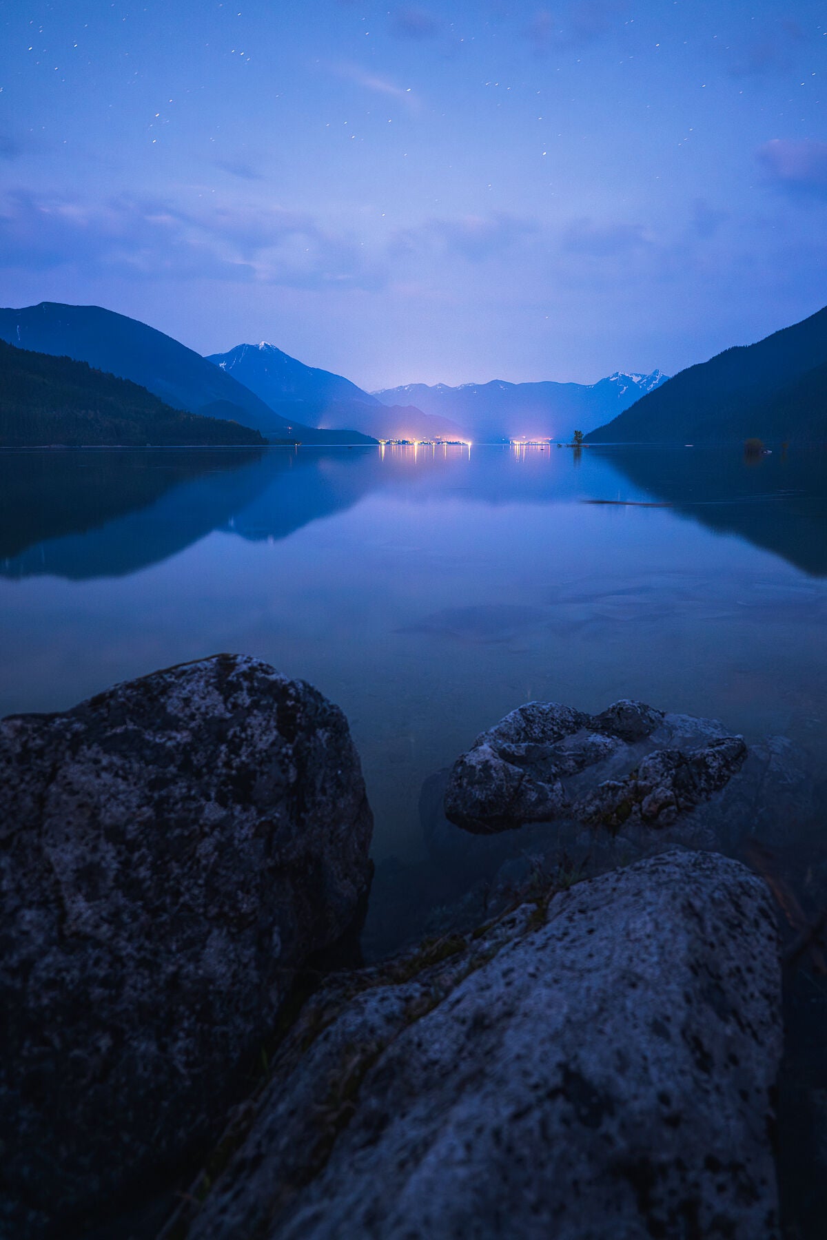 A landscape photo of Slocan Lake, with the lights of New Denver and Silverton visible in the evening light, fine art landscape print by Ashley Voykin