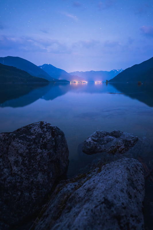 A landscape photo of Slocan Lake, with the lights of New Denver and Silverton visible in the evening light, fine art landscape print by Ashley Voykin