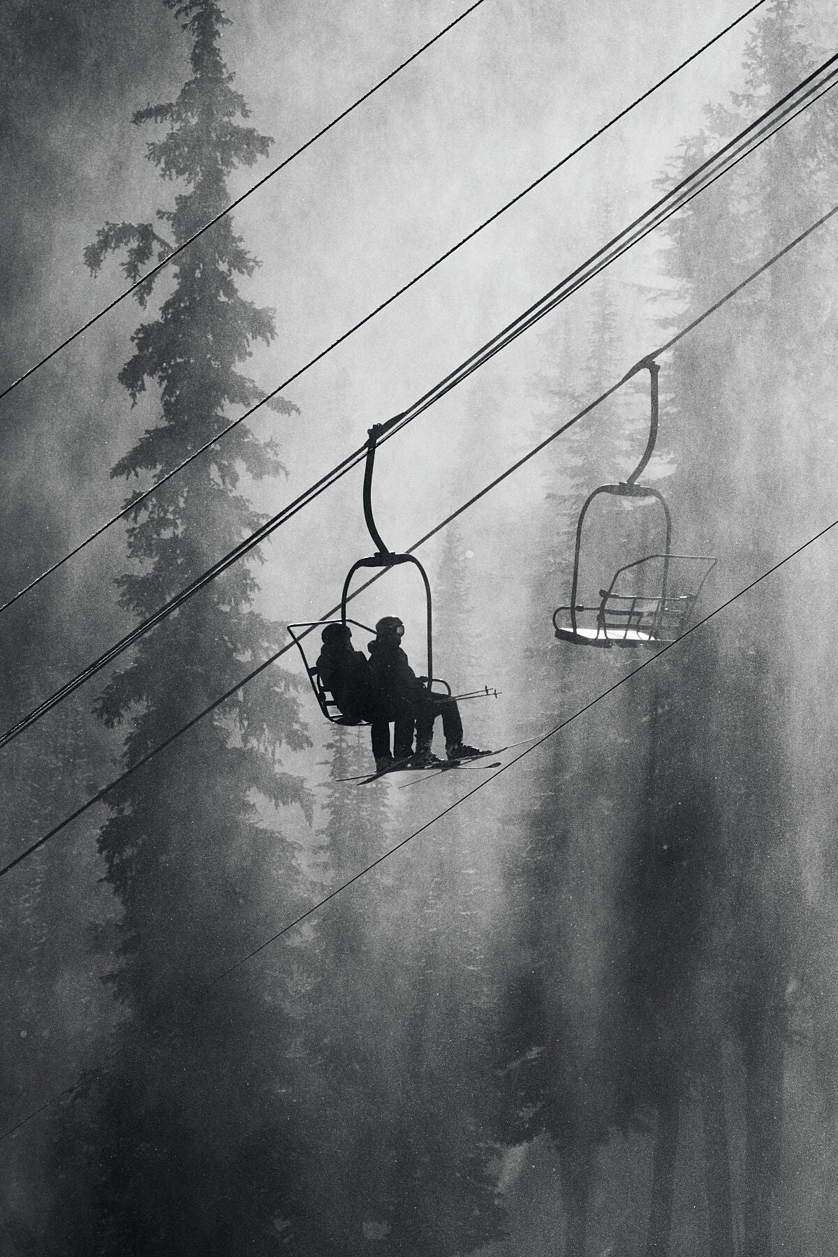 The Motherlode Chairlift at RED Mountain Resort in British Columbia's Monashee Mountains in black and white, two skiers silhouetted against the winter trees. Photograph by Ashley Voykin.