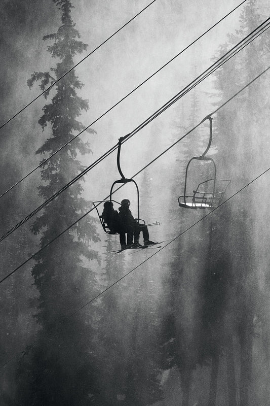 The Motherlode Chairlift at RED Mountain Resort in British Columbia's Monashee Mountains in black and white, two skiers silhouetted against the winter trees. Photograph by Ashley Voykin.